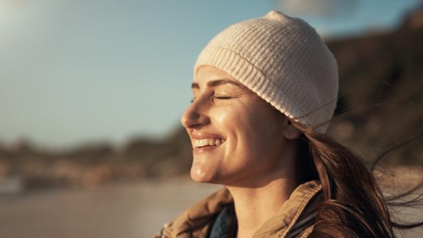 Eine lächelnde Frau mit Mütze genießt die Sonne am Strand.