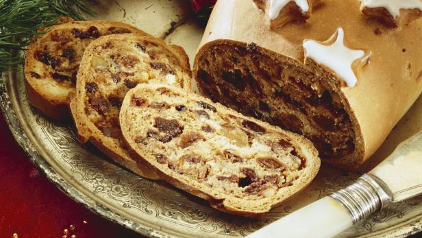 Ein angeschnittener Weihnachtsstollen mit Zimtsternen und einem Weihnachtsmann auf einem Teller.