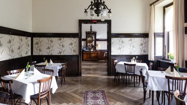 Ein Speisesaal mit gedeckten Tischen und einem Blick in einen angrenzenden Raum.