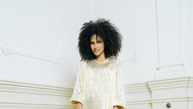 Eine Frau in einem goldenen Kleid mit einer goldenen Handtasche und einem Paket.