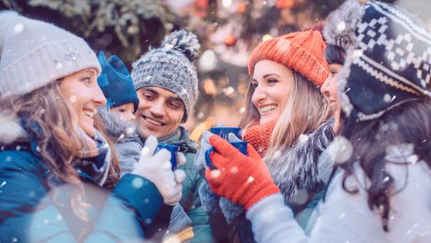 Eine Gruppe von Freunden genießt gemeinsam Glühwein auf einem Weihnachtsmarkt.