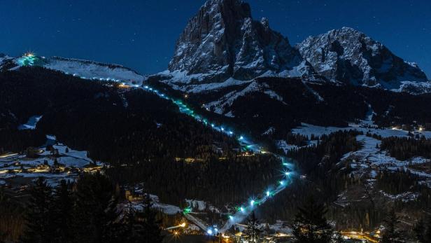Eine Skipiste schlängelt sich nachts beleuchtet einen Berg hinab.