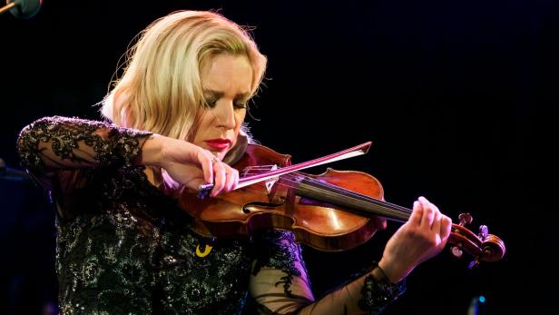 Eine Frau mit blonden Haaren spielt auf einer Bühne Geige.