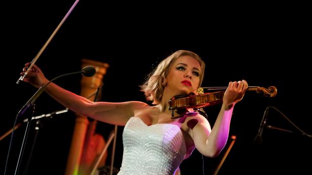 Eine Geigerin spielt in einem weißen Kleid auf der Bühne.