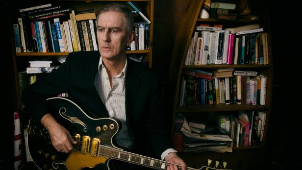 Robert Forster Der Singer-Songwriter Robert Forster posiert vor seinem Bücheregal.
