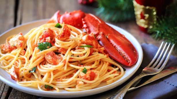 Ein Teller Spaghetti mit Hummersauce und einer Hummerschere liegt auf einem Tisch.