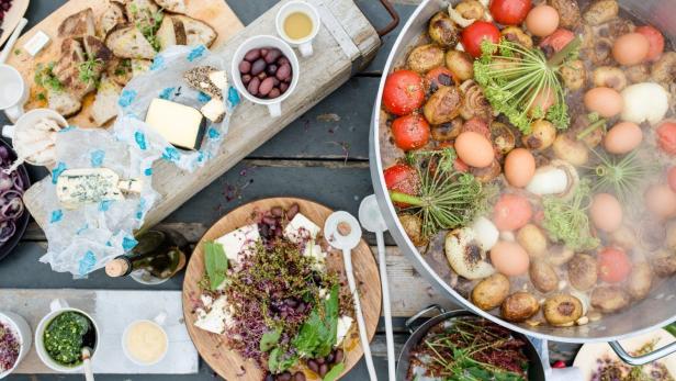 Ein Tisch mit verschiedenen Speisen, darunter Brot, Käse, Salat und ein großer Topf mit Gemüse und Eiern.
