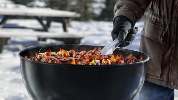 Ein Mann grillt Steaks und Gemüsespieße im Winter.
