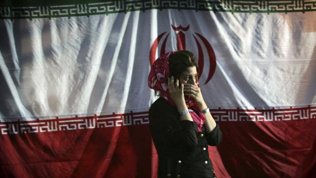 An Iranian girl talks on her mobile phone in front of the national flag at a campaign centre in Tehran June 6, 2005. Picture taken June 6, 2005. To match Special Report IRAN/TELECOMS REUTERS/Damir Sagolj/Files (IRAN - Tags: BUSINESS TELECOMS)