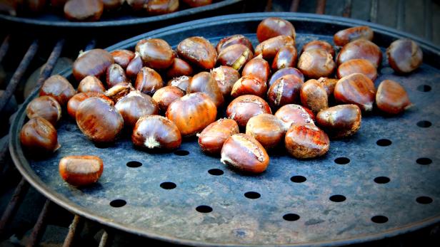 Geröstete Kastanien liegen auf einem perforierten Blech.