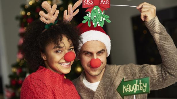 Ein Paar mit roten Nasen und Weihnachtskopfschmuck posiert vor einem Weihnachtsbaum.