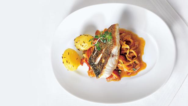 Ein Teller mit Fischfilet, Kartoffeln und einer Sauce mit Zwiebeln und Kräutern.