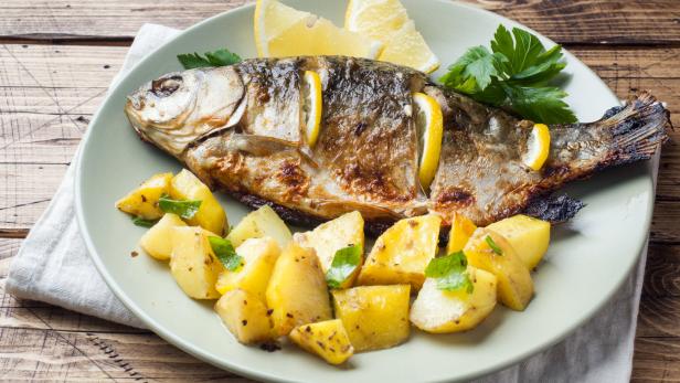 Ein gebratener Fisch mit Zitronenscheiben und Kartoffeln auf einem Teller.