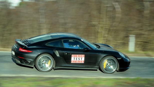Ein schwarzer Porsche mit „Kurier Test Kurier“-Aufklebern fährt auf einer Straße.