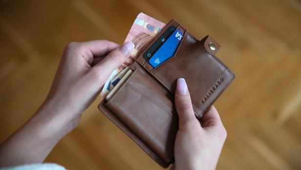 Eine Person hält eine braune Ledergeldbörse mit Geldscheinen und Karten in der Hand.