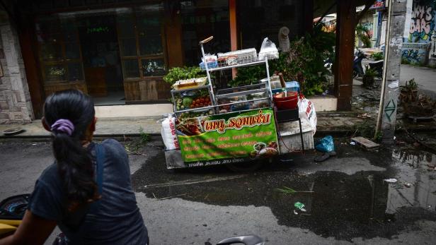 Eine Frau steht vor einem thailändischen Imbisswagen auf der Straße.