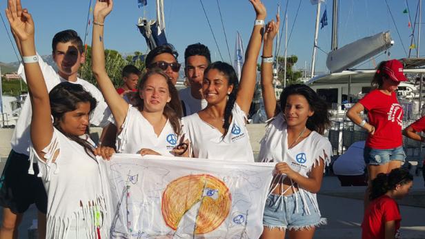 Eine Gruppe junger Leute demonstriert mit einem selbstgemalten Transparent in einem Hafen.