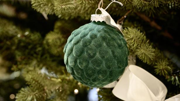 Eine grüne, samtartige Weihnachtskugel hängt an einem Weihnachtsbaum.