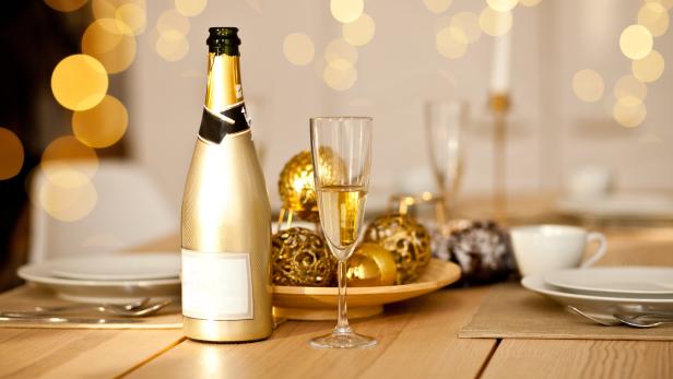 Eine goldene Champagnerflasche und ein Glas stehen auf einem festlich gedeckten Tisch.