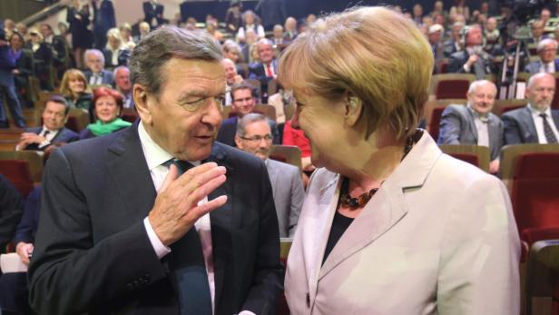 Gerhard Schröder und Angela Merkel unterhalten sich vor Publikum.