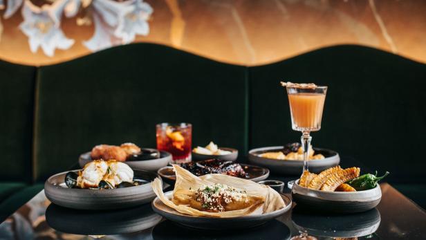 Eine Auswahl an Speisen und Getränken, darunter ein Tamale, Cocktails und Maiskolben.