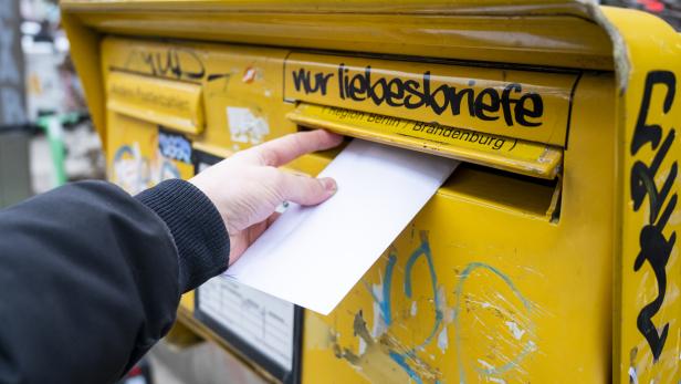 Hand wirft Brief in einen Briefkasten
