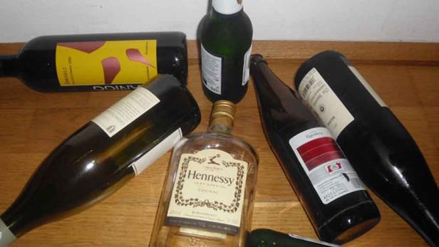 Mehrere leere Flaschen Wein, Sekt und eine Flasche Hennessy Cognac liegen auf einem Holzboden.
