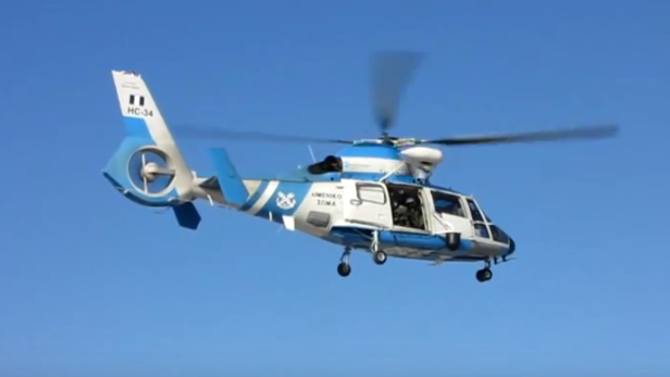Ein blau-weißer Hubschrauber vom Typ HC-34 fliegt vor blauem Himmel.