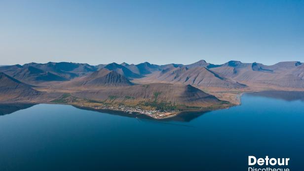 Luftaufnahme einer kleinen Stadt an der Küste mit Bergen im Hintergrund.