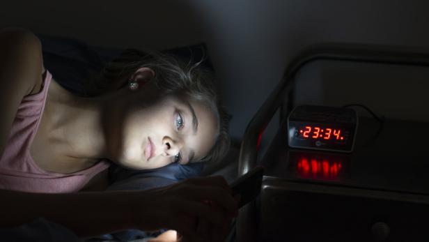Eine junge Frau starrt mitten in der Nacht auf ihr Handy.