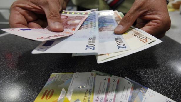 Hände halten Euroscheine; Schweizer Franken liegen auf einem Tisch.