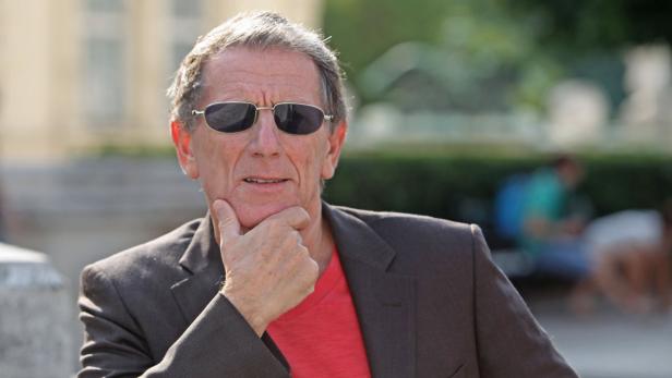 Ein Mann mit Sonnenbrille und Anzug posiert nachdenklich.