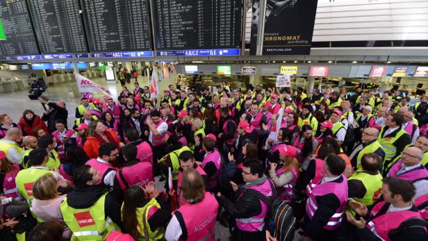 Eine Menschenmenge in Warnwesten und mit Gewerkschaftsfahnen demonstriert in einem Flughafenterminal.
