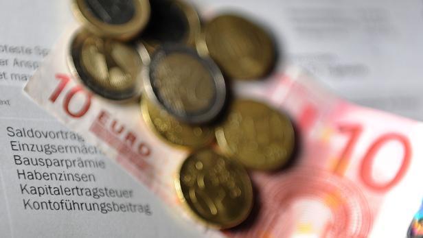 Ein Zehn-Euro-Schein und einige Münzen liegen auf einem Dokument mit Finanzbegriffen.