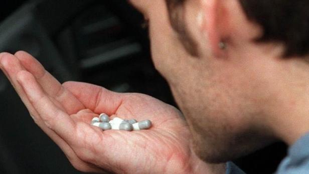 Ein Mann hält Tabletten in seiner Hand.