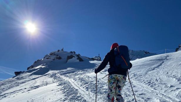 Eine Person steigt mit Skiern und Rucksack einen verschneiten Hang hinauf.