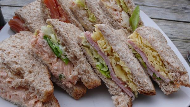 Eine Platte mit verschiedenen Sandwiches, darunter Lachs, Krabben und Schinken mit Käse.