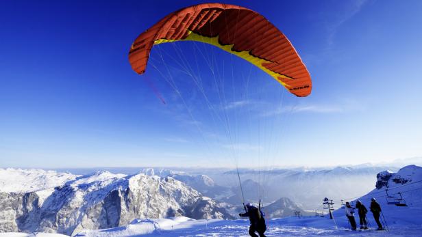 Ein Gleitschirmflieger startet auf einem schneebedeckten Berg mit Blick auf eine Berglandschaft.