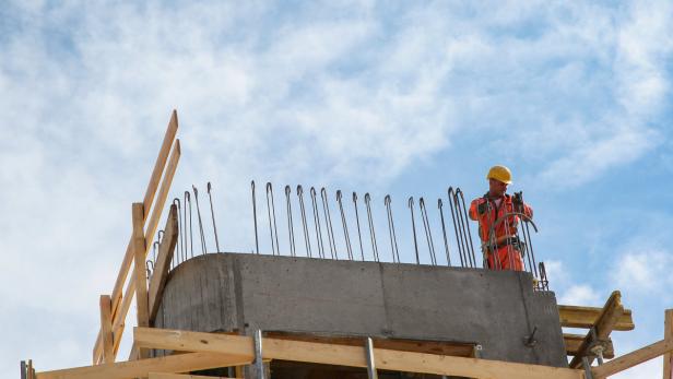 Ein Bauarbeiter mit Helm arbeitet an einem Betonbau mit Bewehrungsstahl.