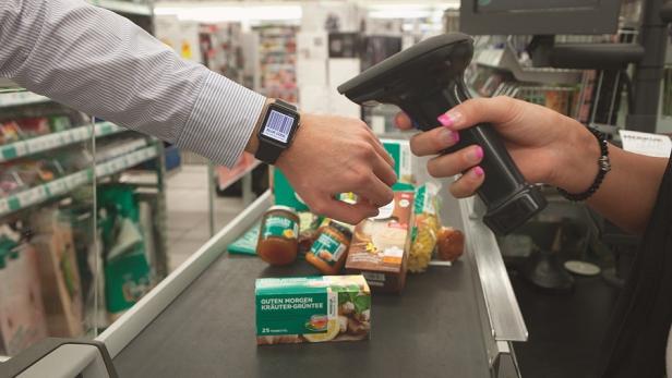 Ein Kunde bezahlt mit einem Barcode auf seiner Smartwatch an der Kasse.