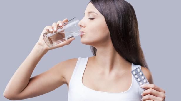 Frau schluckt Antibiotika mit einem Glas Wasser.