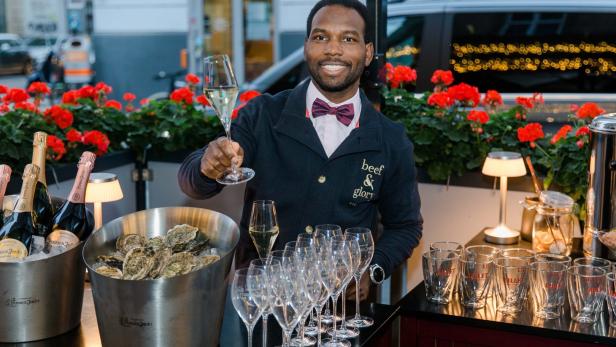 Ein Mann im „Beef & Glory“ hält ein Champagnerglas, Austern und Champagnerflaschen stehen bereit.