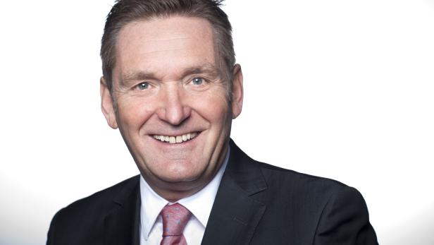 Ein lächelnder Mann im Anzug vor einem weißen Hintergrund.