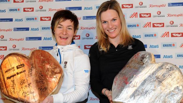 Zwei Sportlerinnen halten herzförmige Auszeichnungen mit Unterschriften in die Kamera.