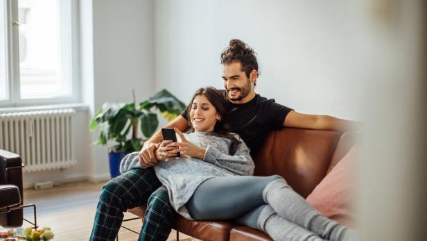 Ein Paar entspannt auf einem Ledersofa und schaut auf ein Smartphone.