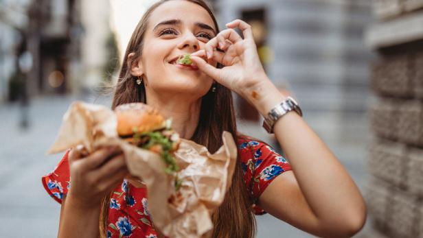 Eine junge Frau isst einen Burger auf der Straße.