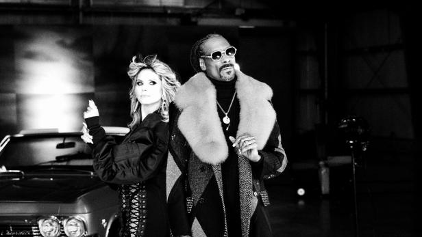Heidi Klum und Snoop Dogg posieren vor einem Oldtimer in Schwarzweiß.