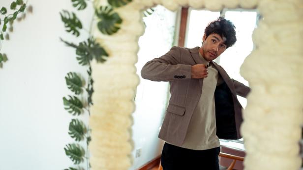 Ein Mann im Blazer betrachtet sich in einem mit Pflanzen geschmückten Spiegel.