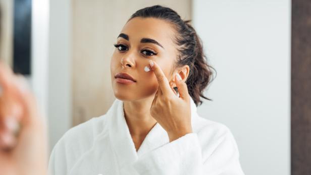Eine Frau im Bademantel trägt Feuchtigkeitscreme auf ihr Gesicht auf.