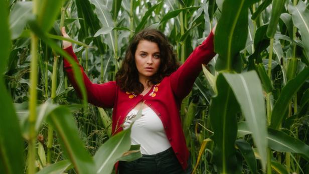 Eine Frau steht in einem Feld aus hohem, grünen Mais.